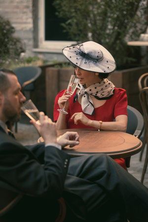 Man and woman sit with champagne and talk softly, dressed in elegant old-fashioned style. Gentle love. Vintage couple in love. Suitable for cover. Concept of vintage, love, nostalgiaの写真素材