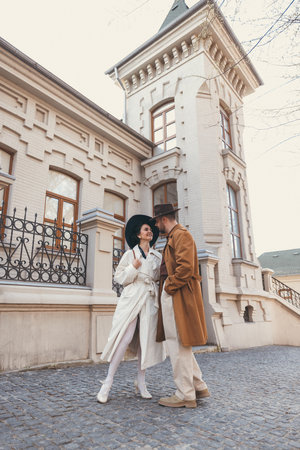 Vintage dressed couple standing close to each other outside historical building, sharing loving glance. Suitable for cover. Concept of elegance and romantic, nostalgia, fashion and style. Adの写真素材
