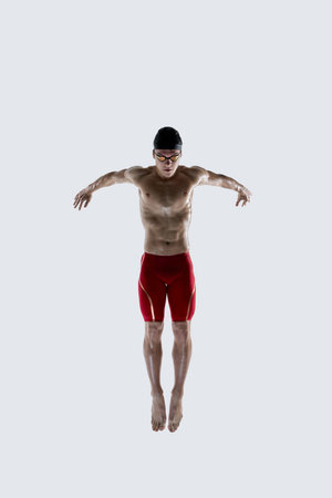 Focused swimmer with powerful forward reach and streamlined body rotates mid-air against white studio background. Concept of strength, speed, tournament, coordination, sports performanceの写真素材