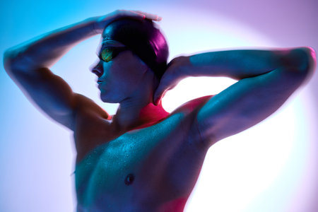 Side view portrait of intense male swimmer gazing forward with neon reflections on face and shoulders against gradient background. Concept of sport, active and healthy lifestyle, competition, trainingの写真素材