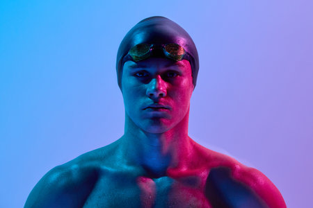 Portrait of intense male swimmer looking at camera with neon reflections on face and body against gradient background. Concept of sport competition, coordination, confidence, tournament.の写真素材