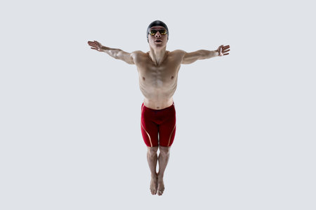 Swimmer with outstretched arms hovers midair with wide gaze and straight legs, showcasing balance, coordination and readiness. Concept of strength, action, concentration, preparation, movementの写真素材