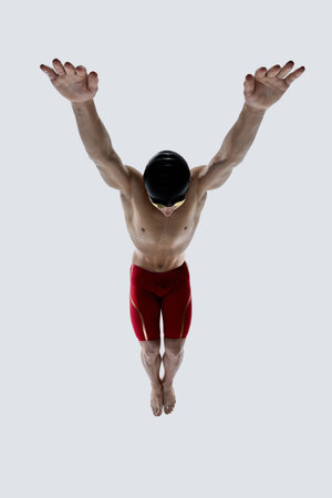 Male swimmer with arms extended wide and head lowered, demonstrating balance, muscle control and preparation for dive against white background. Concept of sport, tournament, focus, motion,の写真素材