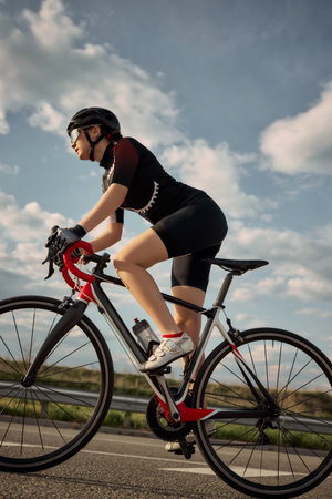 Side view photo of cyclist riding road bike under bright sky, pushing forward on clean highway, captured in golden light with focus on pedaling motion. Concept of freedom, endurance, outdoor.の写真素材
