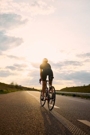 Sporty cyclist riding along highway in evening light, confident posture and silhouette glowing under...