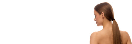 Banner. Rear view of young woman with long straight hair tied in low ponytail and bare healthy back against white background with copy space. Concept of natural beauty, healthy hair, cosmetic productの写真素材