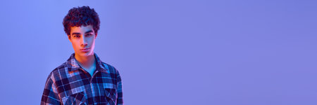 Banner. Teen boy in plaid shirt stares ahead with calm and serious look, posing in neon light...