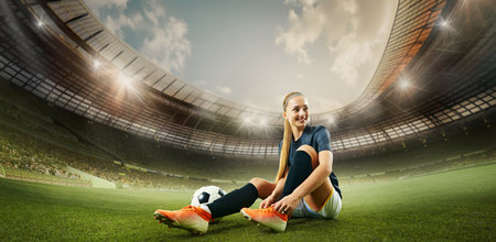 Hand made collage. Female footballer smiles confidently while tying shoes next to ball on bright field, stadium lights glowing above. Concept of sport, football, preparationの写真素材