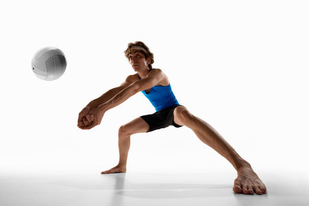 Focused volleyball player in wide stance gets ready to receive ball with tight arms and serious face against white studio background. Low angle. Concept of sport championship, competition, movementの写真素材