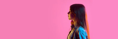 Banner. Side profile of teen girl with calm face in denim jacket under pink neon light against vibrant gradient background. Copy space. Concept of peacefulness, identity, youth, style, emotionの写真素材