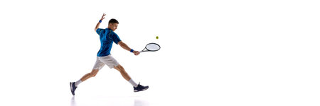 Banner. Young male tennis player jumping and making strong forehand shot in blue-white uniform against white studio background. Copy space. Concept of sport, power strike, athletic movementの写真素材