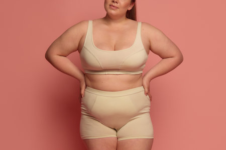 A confident Caucasian woman in comfortable underwear embraces body diversity against a pink background. Concept of self-love, body positivity, and inclusivity.の写真素材
