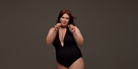 A plus-size woman confidently poses in a stylish black swimsuit, embracing body positivity and self-love. Concept of empowerment and self-acceptance in fashion.の写真素材