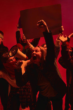 Protesters use a megaphone to shout slogans against a vivid red backdrop, symbolizing struggle and...