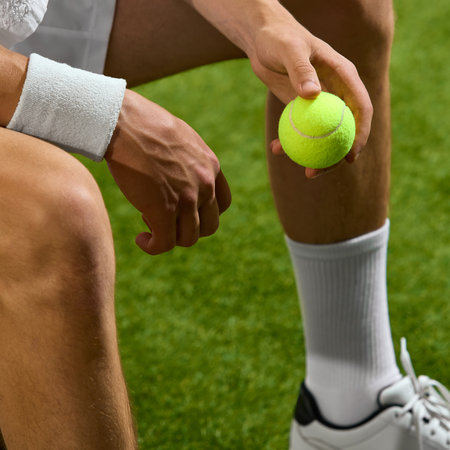 A tennis player sits on a grass court, holding a ball, wearing wristbands and sports shoes, preparing for a match. Concept of readiness and athletic focus.の写真素材