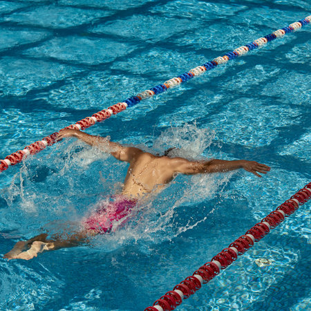 A swimmer performs the butterfly stroke in an outdoor swimming pool lane on a sunny day. Concept of athletic training and swimming technique.の写真素材