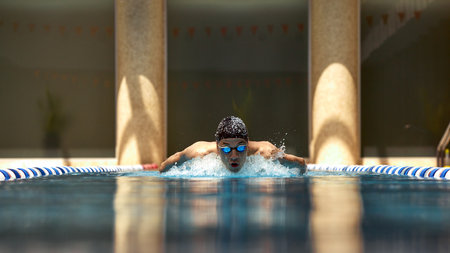 A competitive swimmer performs the butterfly stroke in an indoor swimming pool. Concept of strength and precision in aquatic sports.の写真素材