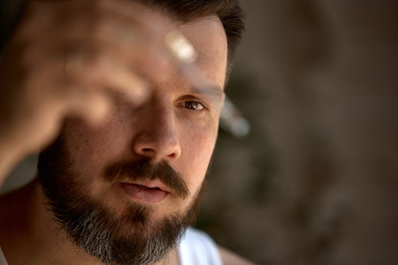 Middle-aged Caucasian man intensely examines a small object under natural light. Concept of meticulous observation and attention to detail.の写真素材