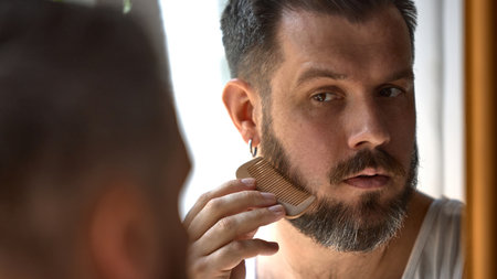 Clean-boy grooming. Man trims, styles his beard with focus and precision. Concept of personal grooming and self-care routine for men.の写真素材