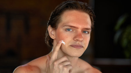 Skin-realism. Smiling man with sun-kissed forehead, shoulders, applying facial moisturizer. Concept of daily personal care and male grooming practices.の写真素材