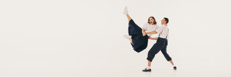 Two people performs an energetic lindy hop dance with dynamic poses against a white studio...