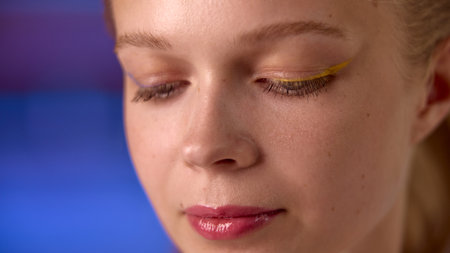 Dopamine makeup. A woman with artistic yellow eyeliner poses against a soft blue background. Concept of bold makeup style and beauty contrast in fashion photography.の写真素材