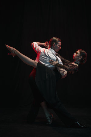 Dancers execute a passionate, elegant Argentine tango pose against a striking dark backdrop. Concept of cultural expression and grace in movement.の写真素材