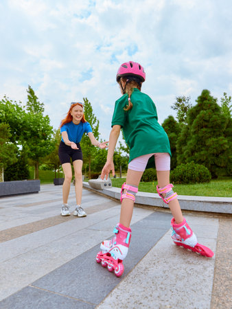 First ride. Young girl is taught roller skating under mother supervision in a park, concentrating on skill enhancement and the enjoyment of outdoor activities. Concept of family recreation timeの写真素材