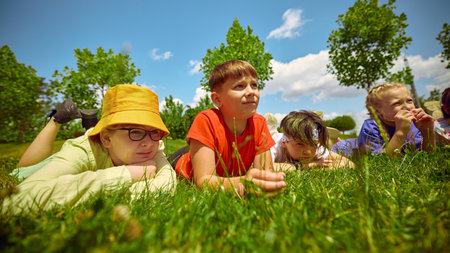 Children rest on the grass beneath a sunny sky in the park, enjoying the warmth and the beauty of...