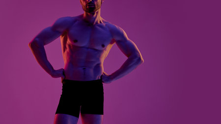 A man with a muscular build stands confidently in front of a lively purple backdrop. Concept of vulnerability, introspection, and quiet masculine emotion in fashion pose.の写真素材
