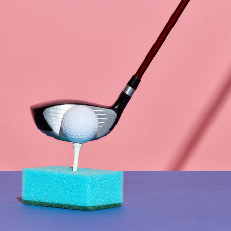 Golf club about to strike ball positioned on tee inserted in blue kitchen sponge. Concept of surreal...