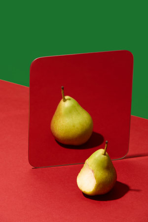 Bitten pear looking into mirror sees full untouched fruit reflection. Concept of idealization, memory, self-perception for health, therapy and food campaign visuals.の写真素材