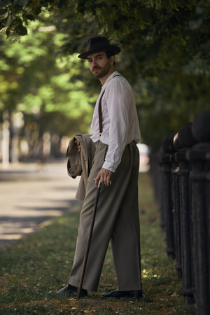 Man in vintage attire walks on tree-lined street under sunlight. Concept of art-based campaigns for...