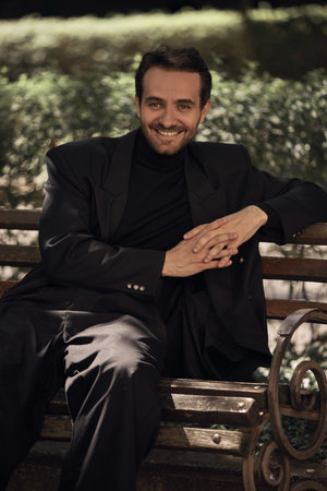 Man in formal attire smiles while sitting relaxed on a park bench under greenery. Concept of cinematic retro portraits, book covers for literary fiction, novellas, and historical narrativesの写真素材