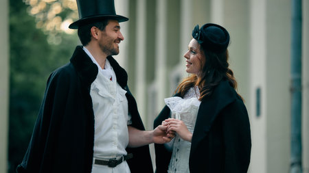 Smiling couple in vintage costume holding hands outdoors. Concept of romantic book cover, historical...