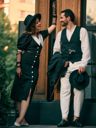 Woman in vintage dress smiling at man leaning on doorway. Concept of historical novel cover, urban...
