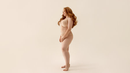 Confident woman with long red hair posing against neutral background. Concept of body positivity, powerful femininity, stylish bodywear, fashion confidence, bold character in underwear marketing.の写真素材