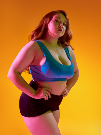 Self-assured woman posing against lively orange background. Concept of vivid body expression, radiant energy in fashion campaigns, confident sportswear identity.の写真素材