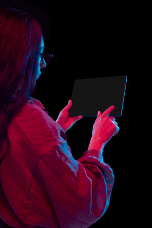 Close-up of woman holding digital tablet with blank screen in neon lighting. Concept of mobile app prototyping, digital interface design, tech tutorials, and user-centered creativity with precision.の写真素材