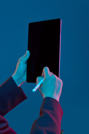 Hands drawing on blank copy space tablet with stylus in blue background. Concept of fintech...