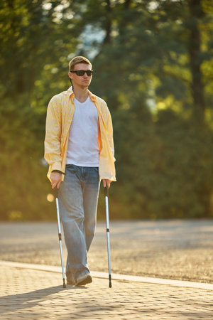 Blind man walking independently on park path using assistive trekking poles. Concept of assistive...
