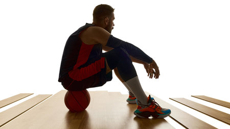 Male basketball athlete resting on ball with thoughtful expression. Concept of health awareness, recovery, coaching moments, publishing content, sports attitude in training breaks.の写真素材