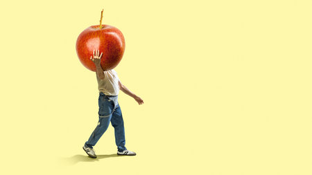 Collage of a man walking with giant apple on yellow background. Concept of nutrition awareness, healthy lifestyle, seasonal fruit identity, and playful wellness.の写真素材