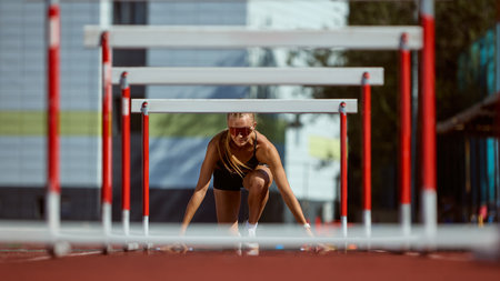 Female hurdler in starting position focused on race. Concept of anticipation, strength, resilience, mental clarity, and determination to overcome challenges.の写真素材