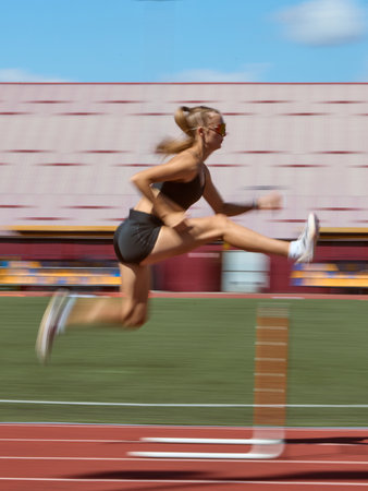 Female hurdler in fast motion blur over hurdle on track. Concept of speed, intensity, competition, dynamic movement, strength, and athletic spirit.の写真素材