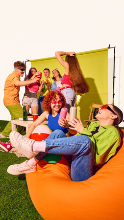 Group of young friends laughing and drinking on beanbags with green backdrop. Concept of carefree...