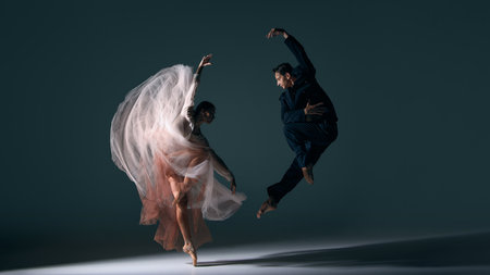 Ballet couple moving in synchronized dramatic jump with flowing dress motion. Concept of energy, passion, performing arts, fluid choreography, emotional harmony and cultural expression.の写真素材