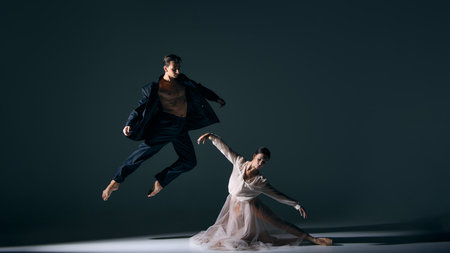 Male dancer leaping high as female ballerina bends gracefully. Concept of contrast, energy, elegance, art, and dynamic storytelling in dance.の写真素材