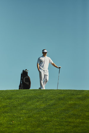 Golfer standing with club and bag on sunny course. Concept of outdoor sport, lifestyle, leisure, health, discipline, and personal achievement.の写真素材