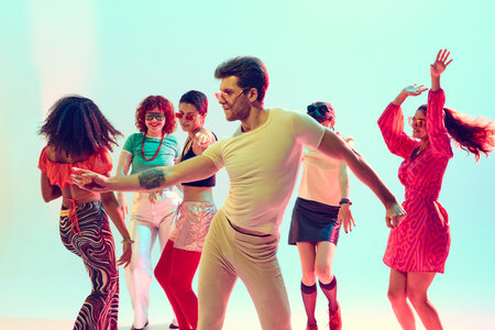 Young man leading retro dance moves with friends in vibrant studio light. Concept of disco culture,...